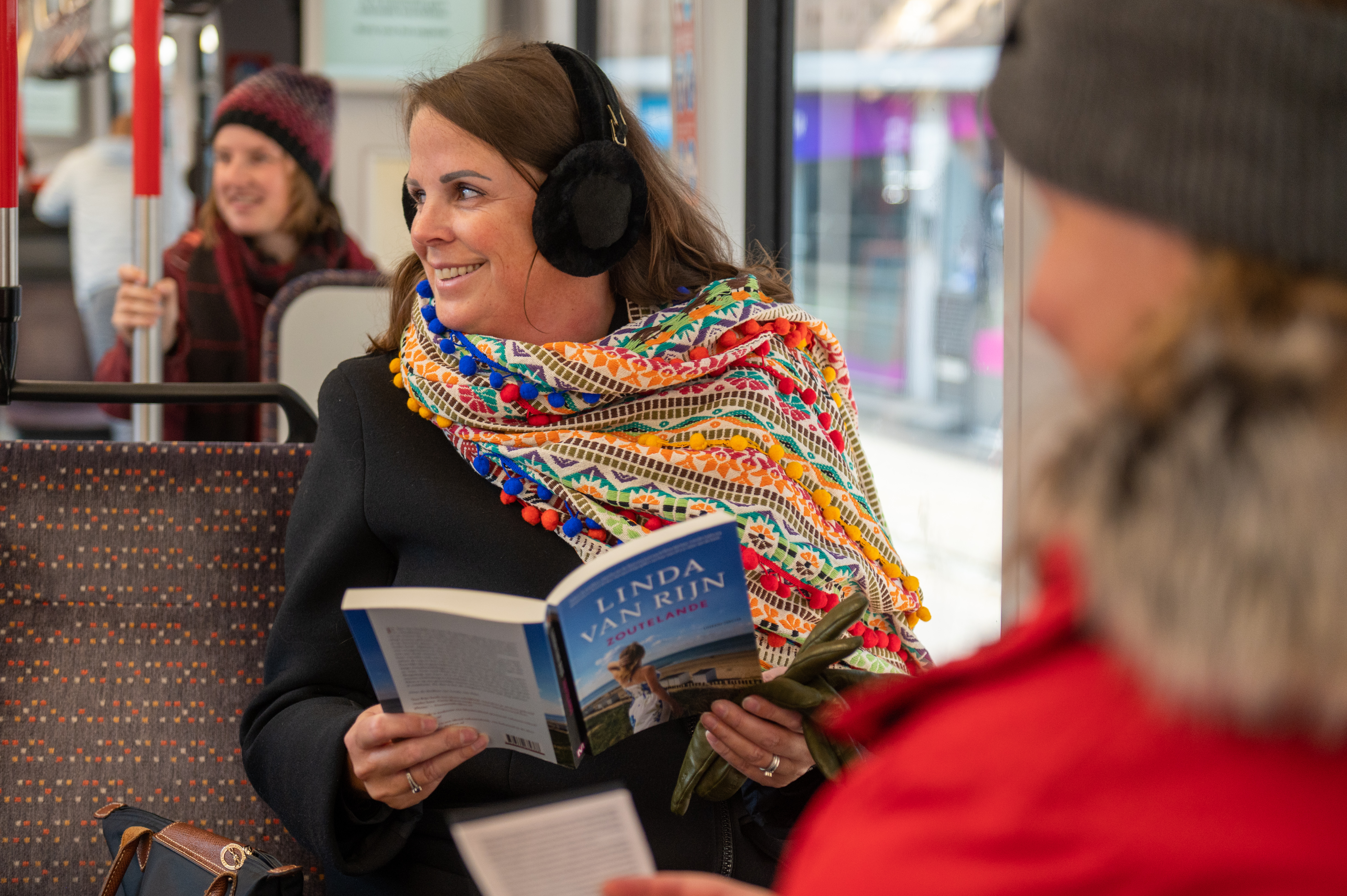Vrouw leest boek in HTM tram en heeft oorwarmers op
